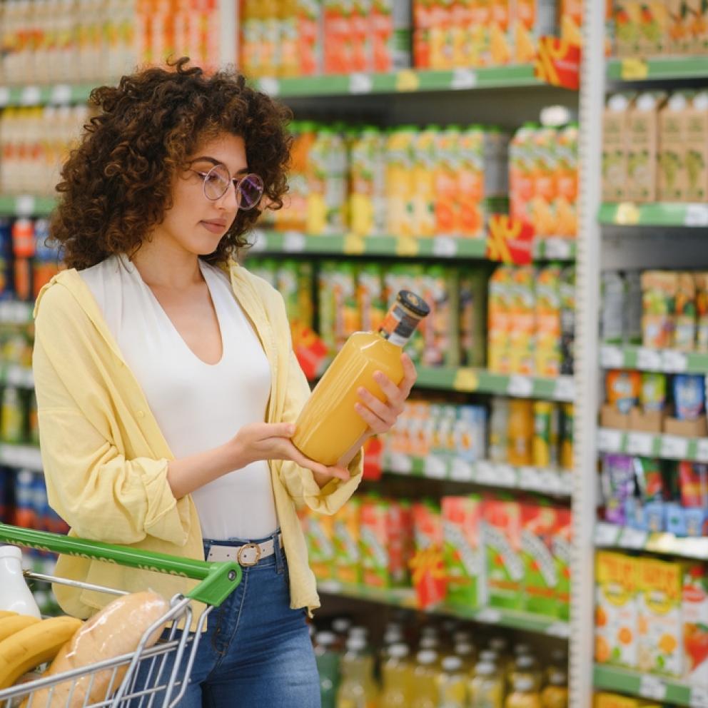 Mujer joven empujando carrito de compras y la elección de la botella de zumo en la sección de supermercados de comestibles
